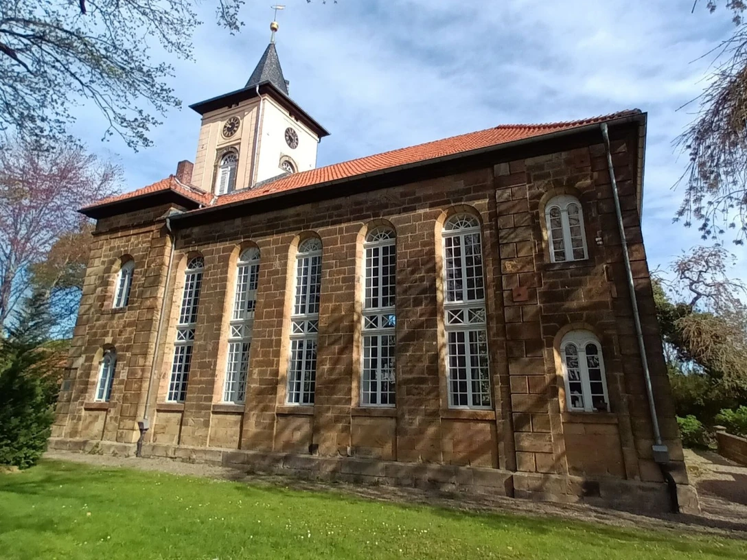 Christuskirche_Gitter (1)_HD_16zu9.jpg Historische Sandsteinkirche mit hohen Rundbogenfenstern, Turm mit Uhr und Spitzdach im Grünen.