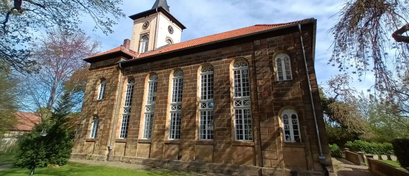 Christuskirche_Gitter (1)_HD_16zu9.jpg Historische Sandsteinkirche mit hohen Rundbogenfenstern, Turm mit Uhr und Spitzdach im Grünen.
