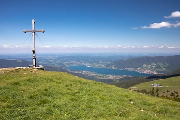 Gipfelkreuz auf dem Hirschberg mit Blick auf den Tegernsee. Gipfelkreuz auf dem Hirschberg, Bayern, mit Blick zum Tegernsee