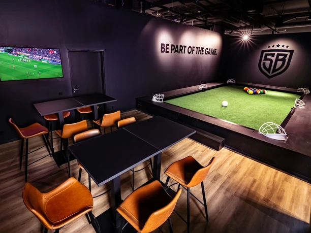 SOCCERBEAT - Spielzone Interaktive Spielfläche mit Sitzbereichen und Blick auf einen großen Bildschirm.