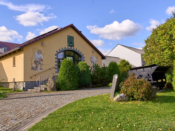 Gelbes Haus mit Torbogen, Bilder an der Wand und gepflastertem Weg.