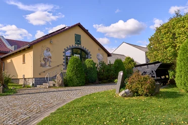 Gelbes Haus mit Torbogen, Bilder an der Wand und gepflastertem Weg.