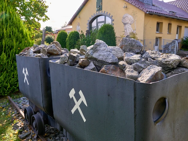 Bergbauwagen Steinen und weißen Kreuzen als Zeichen vor einem Haus und Büschen.