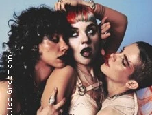 Drei Performer posieren eng nebeneinander mit ausdrucksstarken Gesichtszügen.