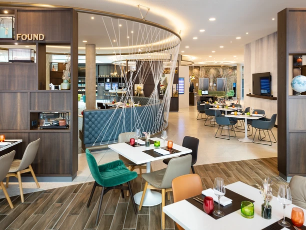 Hyatt Place Frankfurt Airport - Restaurant Restaurant mit modernem Ambiente und farbigen Stühlen an weißen Tischen.