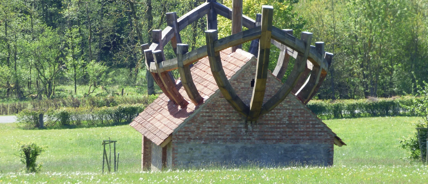 P1170785.JPG Kleines Ziegeldachhaus mit großem Holzschiffgerüst auf dem Dach, umgeben von grüner Wiese und Wald.