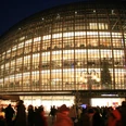 Das Weltstadthaus auf der Schildergasse Das beleuchtete Weltstadthaus in Köln mit geschwungener Glasfassade, umgeben von Menschen.The illuminated Weltstadthaus in Cologne with its curved glass façade, surrounded by people.