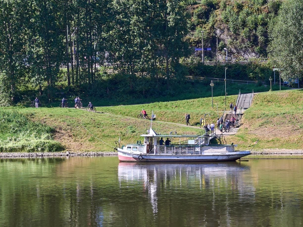 Anlegestelle Schmilka-Hirschmühle Boot mit Personen auf Fluss, Menschen am Ufer und Bäume im Hintergrund.