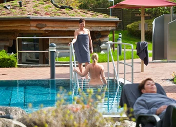 Damensauna Two women relax in the outdoor area with pool and sauna, surrounded by peaceful nature.