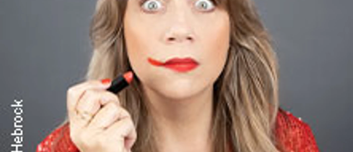 Mirja Regensburg hält einen Lippenstift, der im Gesicht verstrichen ist, vor grauem Hintergrund.
