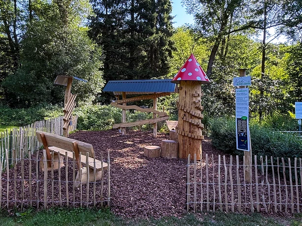 Holzspielplatz mit Murmelbahn und Pilzturm im Grünen Neustadt, umgeben von Bäumen und Holzzaun.