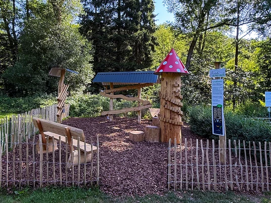 Murmelbahn Neustadt Holzspielplatz mit Murmelbahn und Pilzturm im Grünen Neustadt, umgeben von Bäumen und Holzzaun.