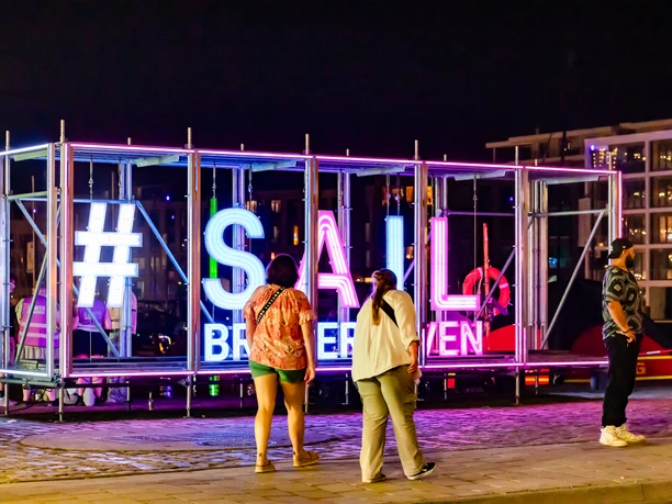 CAL_0584 (99) (c) Carmen Lindemann_Erlebnis Bremerhaven_CC0.jpeg Leuchtende #SAIL Bremerhaven-Installation bei Nacht, umgeben von Besucherinnen und Besuchern.