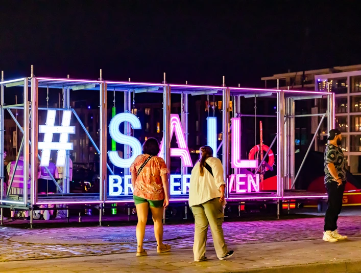 CAL_0584 (99) (c) Carmen Lindemann_Erlebnis Bremerhaven_CC0.jpeg Leuchtende #SAIL Bremerhaven-Installation bei Nacht, umgeben von Besucherinnen und Besuchern.