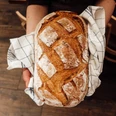 frisches Brot_Bäckerei Ripken.jpeg Frisch gebackenes Brot mit goldbrauner Kruste wird in einem Tuch auf Händen gehalten.