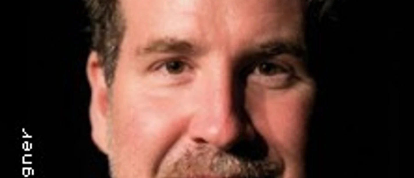 Porträt von Torsten Schlosser vor schwarzem Hintergrund, lächelnd.