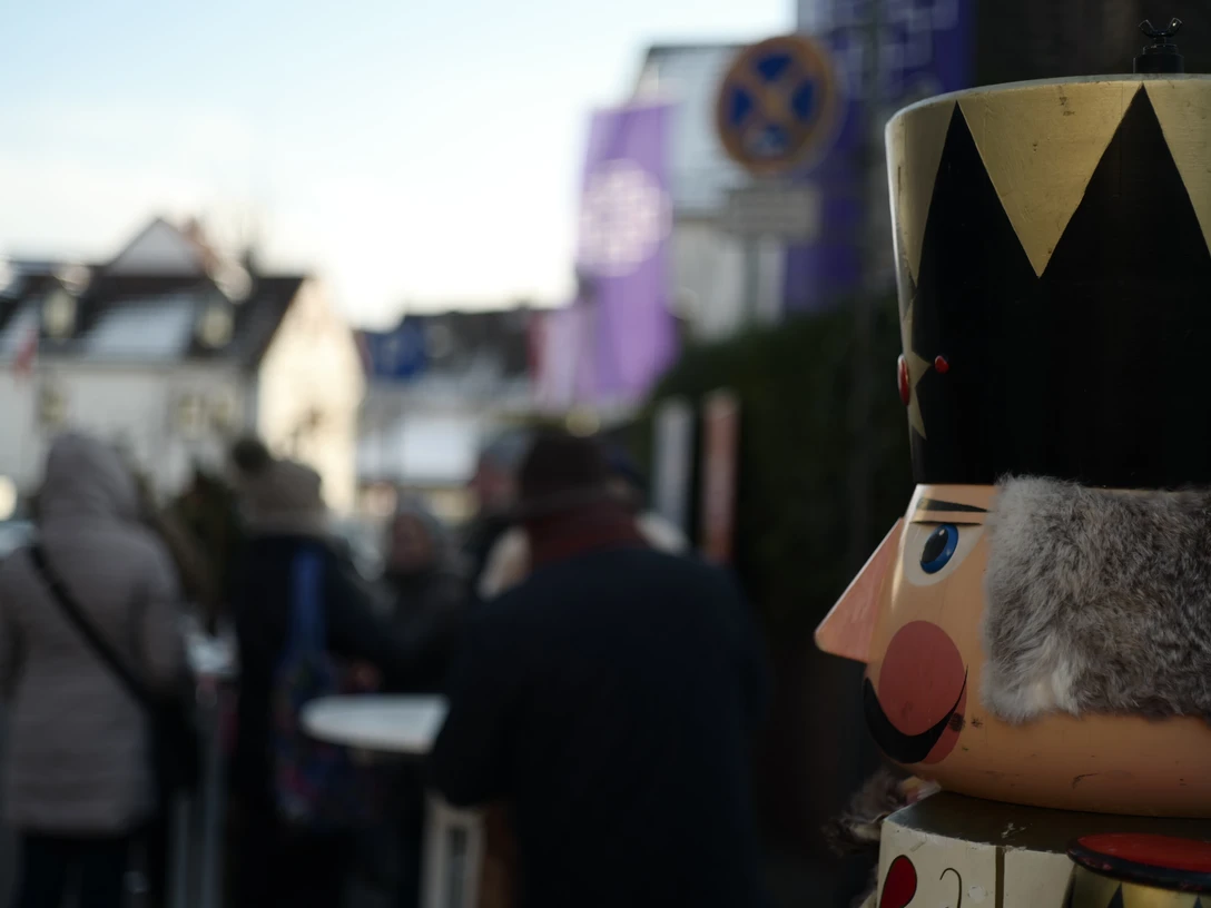 FDorf Seulberg Nikolausmarkt .JPG Im Vordergrund ist ein traditioneller Nussknacker zu sehen, der sich die Menschen auf dem Nikolausmarkt im Hintergrund ansieht. Der Hintergrund ist unscharf.