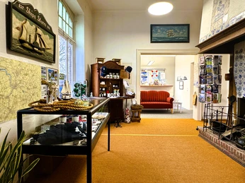 Tourist-Information Rhauderfehn innen.jpg Innenraum der Tourist-Information Rhauderfehn mit Vitrinen, Modellschiff, rotem Sofa, Prospektständer und Kamin.