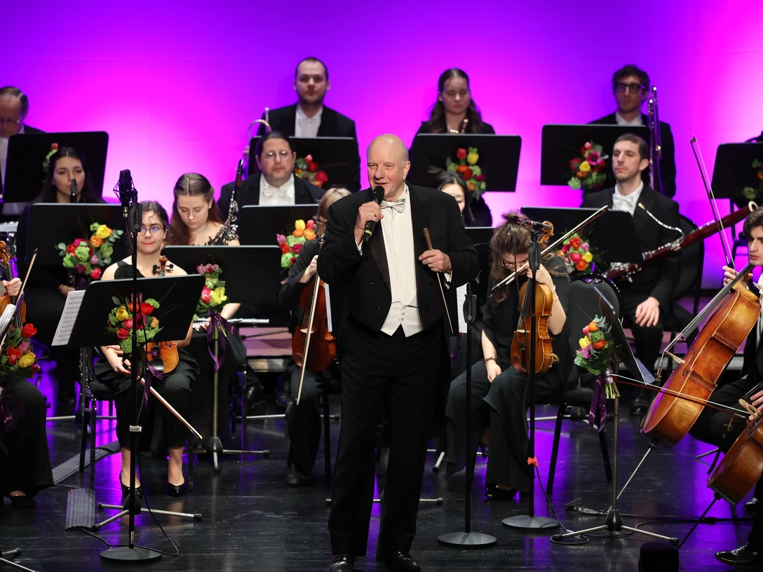 Junge Philharmonie Köln zu Gast in Espelkamp Dirigent der Jungen Philharmonie Köln spricht vor dem Orchester auf Bühne mit violetter Beleuchtung.