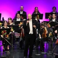 Junge Philharmonie Köln zu Gast in Espelkamp Dirigent der Jungen Philharmonie Köln spricht vor dem Orchester auf Bühne mit violetter Beleuchtung.