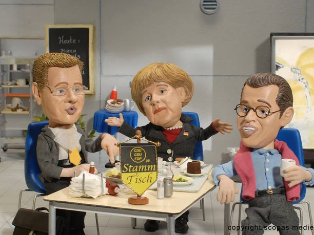 Trickfilmland - Animated characters Three animated characters are sitting together at a round table, in the centre of which is a small pennant with the inscription “Stammtisch”.