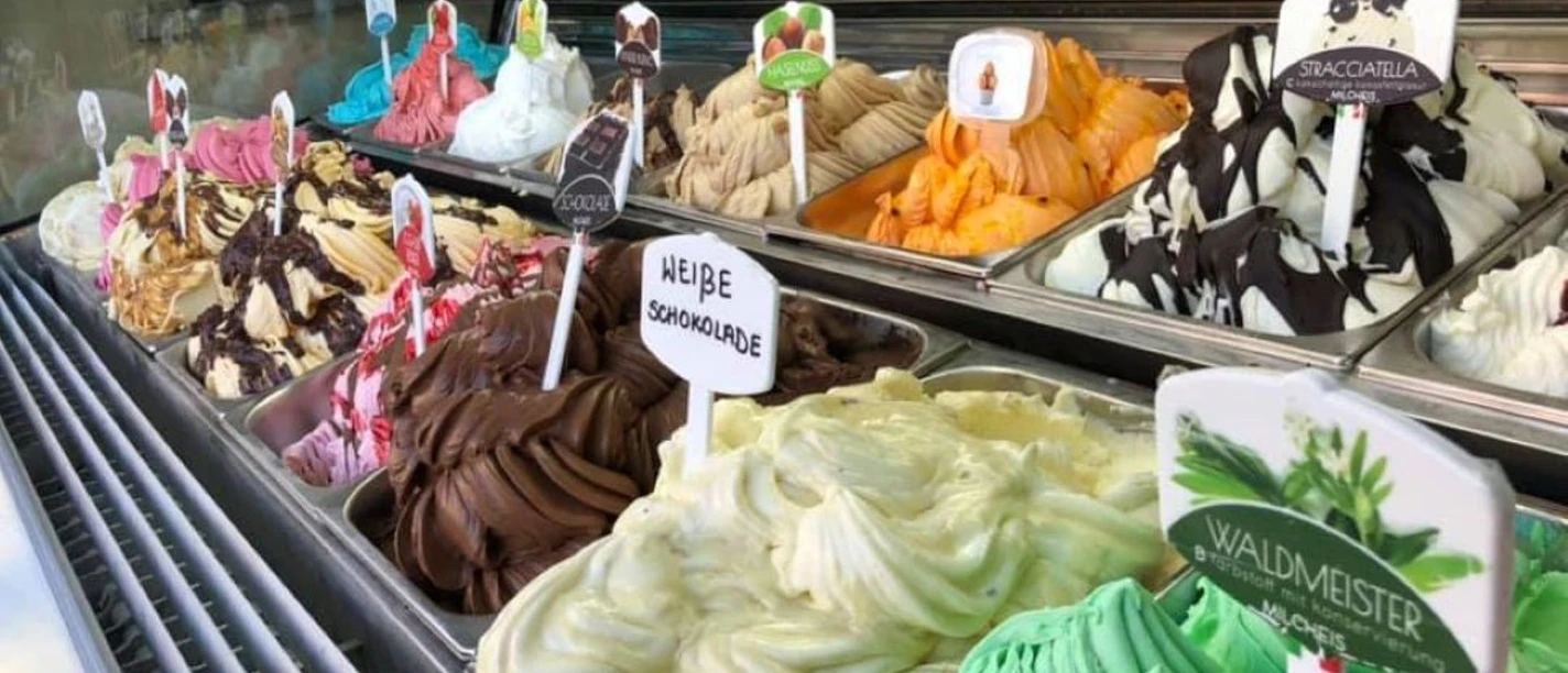 Bunte Eistheke mit verschiedenen Sorten wie Stracciatella, Waldmeister und weißer Schokolade.
