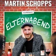 Martin Schopps sitzt vor einer Tafel mit dem Schriftzug "Elternabend", umringt von Wein.