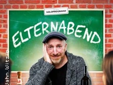 Martin Schopps sitzt vor einer Tafel mit dem Schriftzug "Elternabend", umringt von Wein.