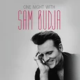 Porträt eines lächelnden Mannes, der auf einem monochromen Hintergrund posiert, begleitet von Text "One Night With Sam Budja".