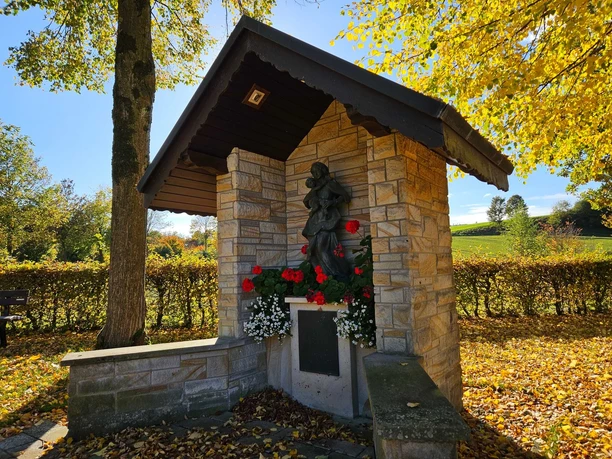 Steinerner Bildstock mit Marienfigur und Blumen, umgeben von herbstlichen Bäumen in Bad Driburg-Erpentrup.