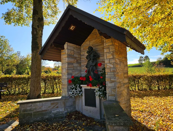 Steinerner Bildstock mit Marienfigur und Blumen, umgeben von herbstlichen Bäumen in Bad Driburg-Erpentrup.