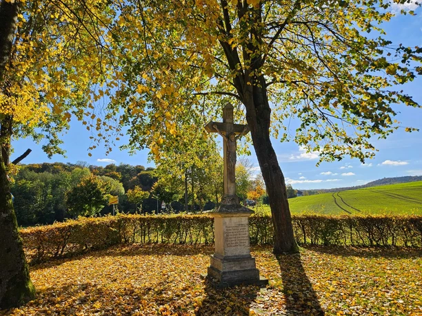 Steinerner Bildstock mit Kreuz unter herbstlichen Bäumen am Feldrand bei Bad Driburg-Erpentrup.