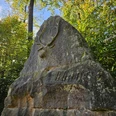 Großer Gedenkstein mit Hirschrelief und Inschrift „BODO“, umgeben von grünem Laubwald.