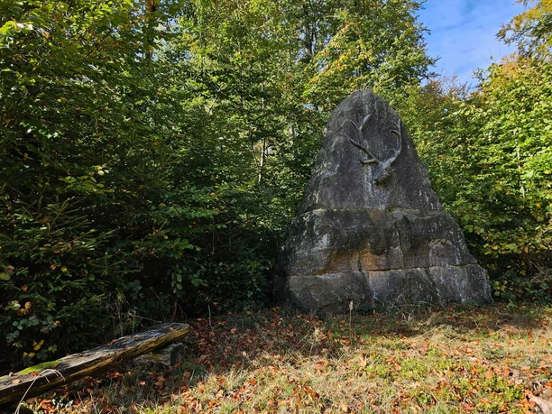 Bad-Driburg Langeland Bodostein Großer Gedenkstein mit Hirschrelief im Wald von Bad Driburg, umgeben von Laubbäumen und Laub am Boden.