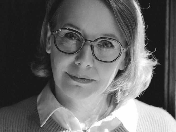 Sandra Lüpkes Webversion.jpg Persoon met schouderlang golvend haar, wit shirt en lichtgrijze trui tegen een donkere achtergrond.