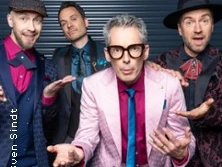 Vier Männer in bunten Anzügen posieren vor einem Garagentor.