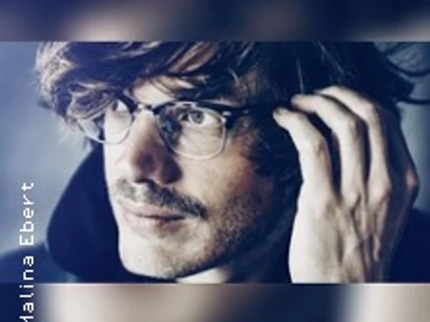 Porträt von Karl Neukauf mit Blick zur Seite, trägt Brille und berührt das Haar.