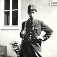 01 Heinrich Jansen_Querformat.jpg Historische Aufnahme eines uniformierten Grenzbeamten mit Gewehr vor einem Gebäude mit Schild.