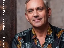 Wladimir Kaminer trägt ein Hemd mit markantem Muster und lächelt in einer entspannten Pose.