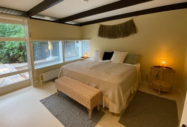 Schlafzimmer Helles Schlafzimmer mit Doppelbett, modernen Deckenbalken, warmem Licht und Blick auf Holzterrasse.