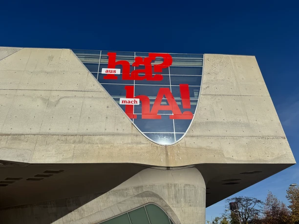 phaeno.jpeg Moderne Betonfassade mit Glasfront und roter Schrift „Hä? aus mach HA!“