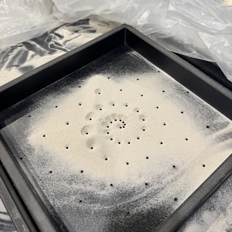 sandschnecke.jpeg Sand in einem Sieb, dessen Löcher angeordnet sind wie ein Schneckenhaus.