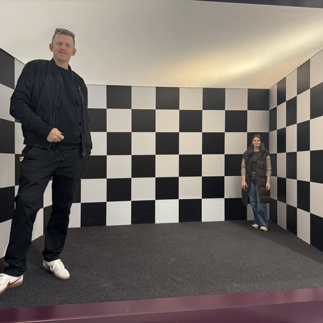 optische Taeuschung.jpeg Zwei Personen stehen in einem Raum mit schwarz-weiß karierten Wänden
