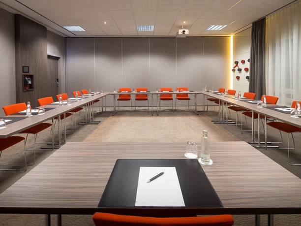Lindner Hotel Frankfurt Höchst - Tagungsraum Duesseldorf Moderner Tagungsraum mit U-Bestuhlung und orangefarbenen Stühlen.