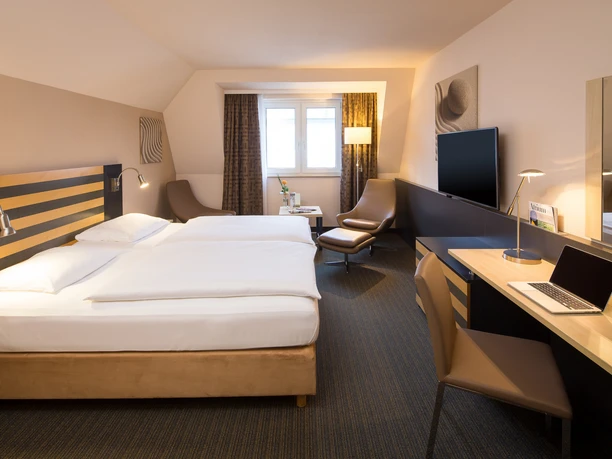 Lindner Hotel Frankfurt Höchst Helles Hotelzimmer mit Doppelbett, Schreibtisch und Lounge-Sessel.