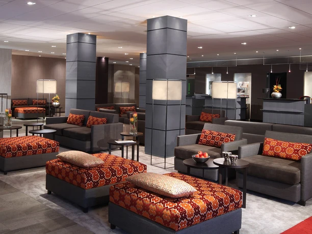 Lindner Hotel Frankfurt Höchst - Lobby Gemütliche Lobby mit grauen Sofas und gemusterten Hockern.