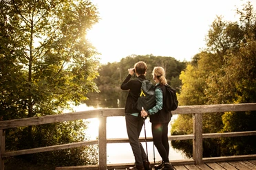 Wandern in der Gruppe (c) TZHS - Anne Weise (14).jpg Zwei Frauen in Wanderkleidung auf Steg mit Blick auf See und Fernglas
