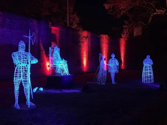 Lumina Rolduc 1 (c) Abdij Hotel Rolduc.jpg Blau und rot leuchtende Ritterfiguren in einem Park vor einer Mauer.