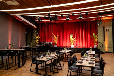 Vogel Event Partner – Interior Design Seated room with covered tables and a stage decorated with plants.