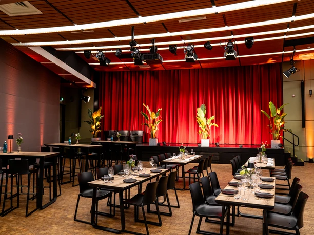 Vogel Event Partner – Interior Design Seated room with covered tables and a stage decorated with plants.